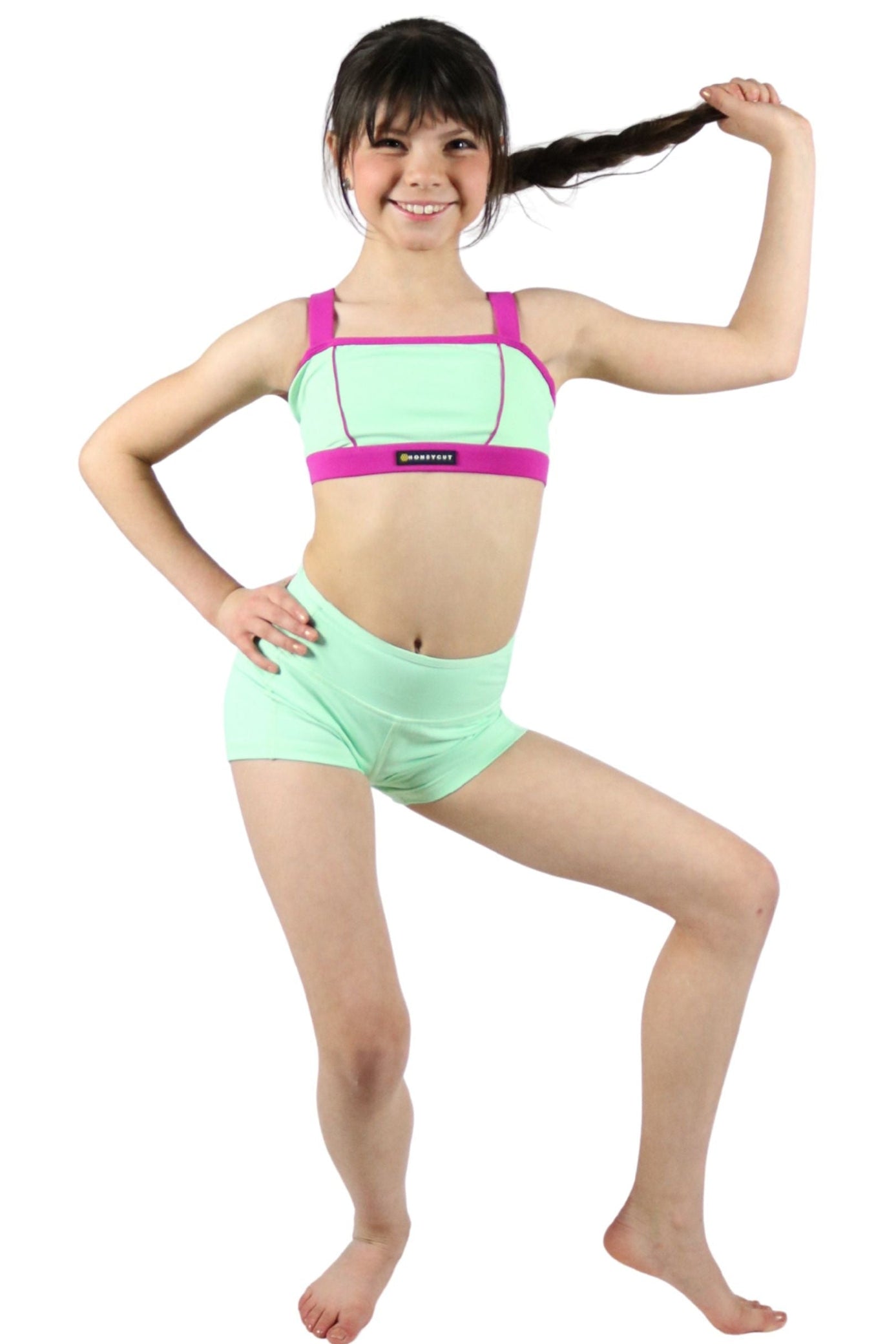 Young girl wearing a green and pink dance outfit on a white background