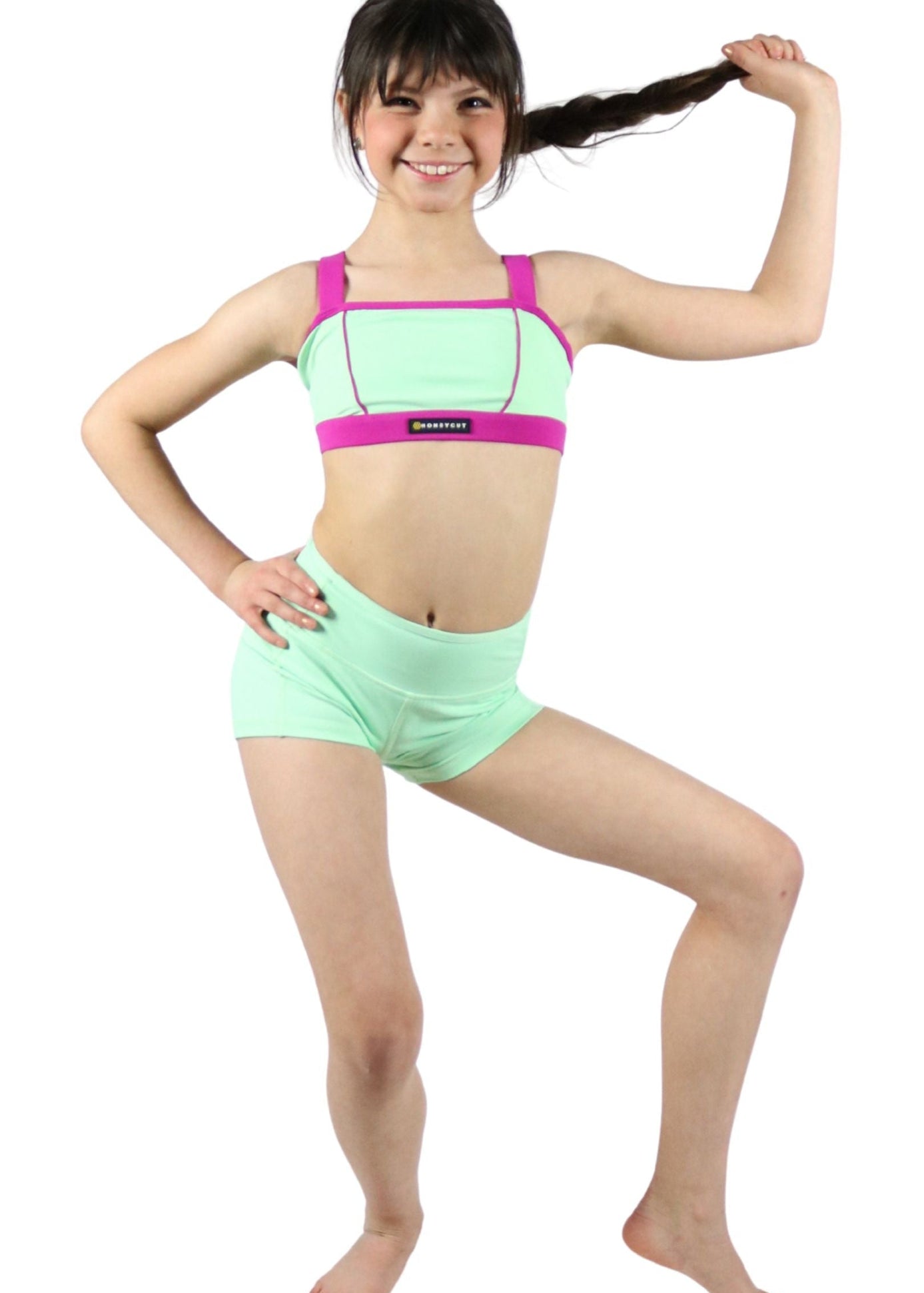Young girl wearing a green and pink dance outfit on a white background