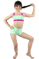Young girl wearing a green and pink dance outfit on a white background
