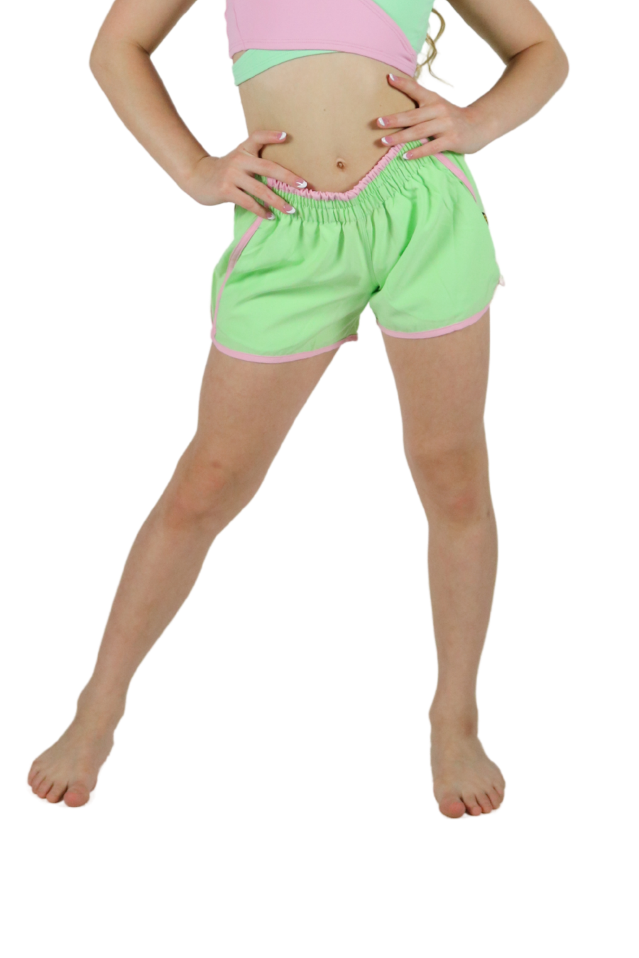 Young girl wearing a pink and green crop top with matching shorts on a white background